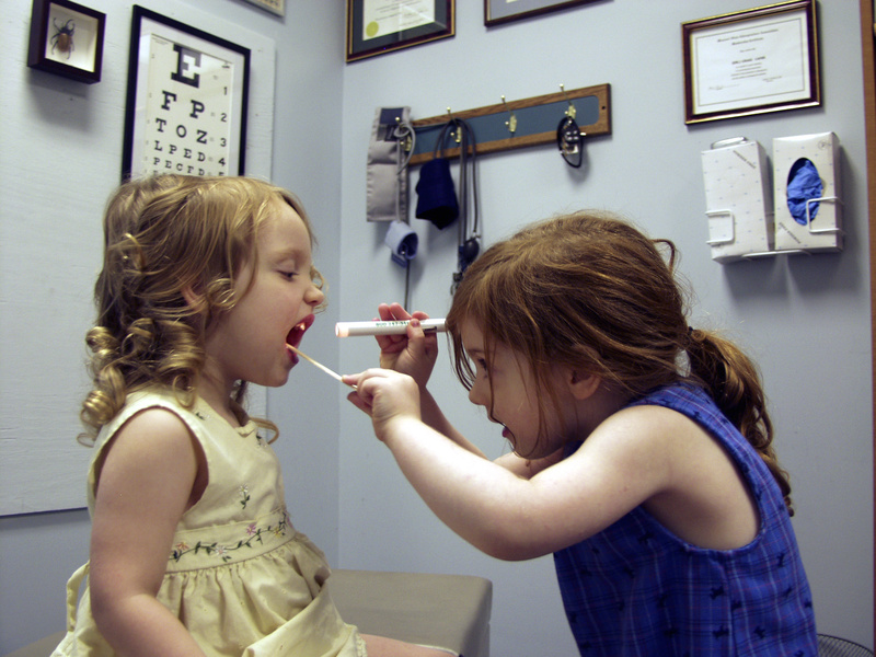 Two little girls playing in a medical office with one girl checking the other one's throat